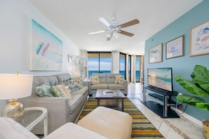 A living room with a sofa, coffee table, TV, and artwork on the walls. - Phoenix V 907 1 Bedroom Condo (Orange Beach)