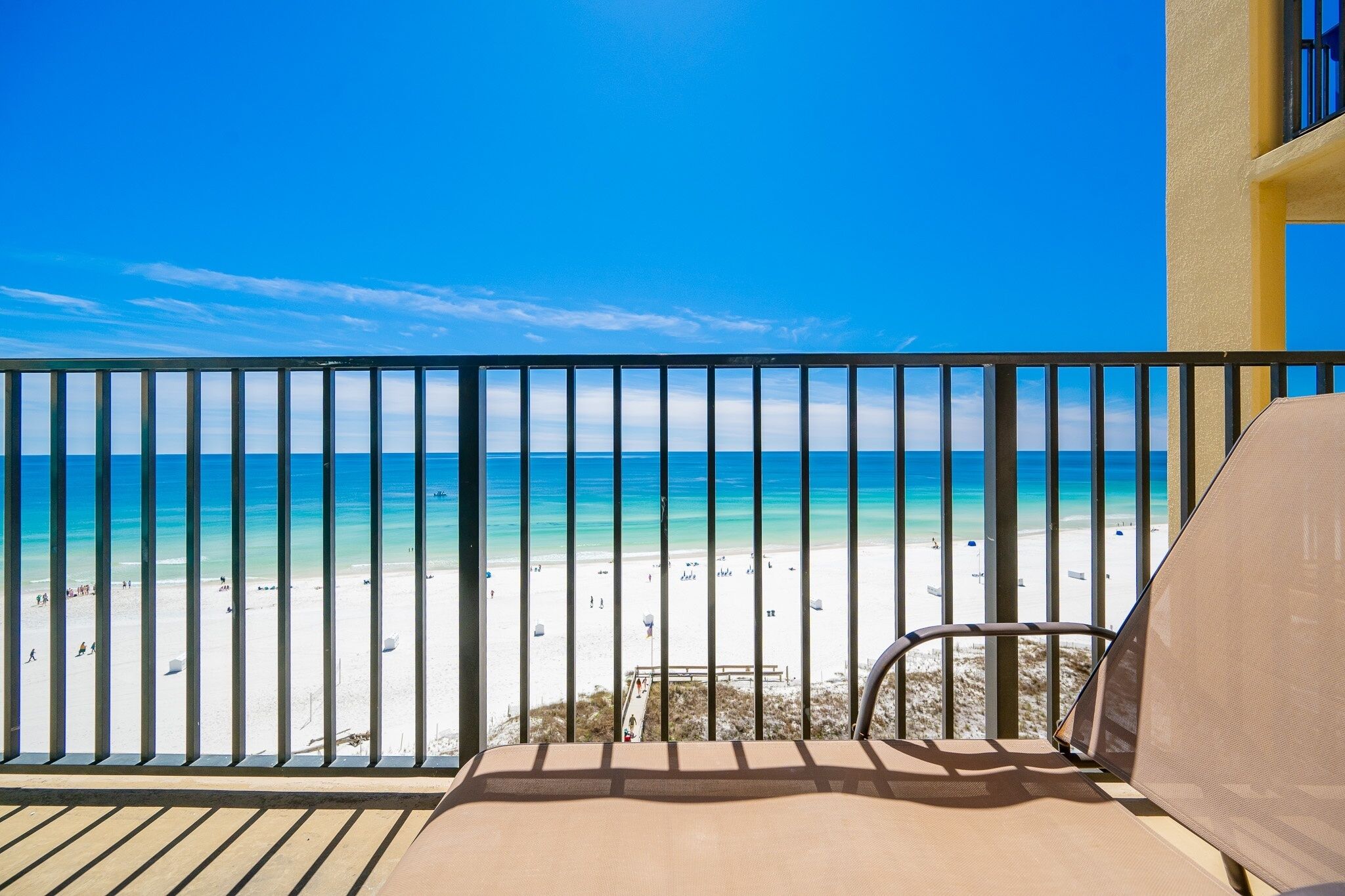 A balcony with a view of a beach, a chair, and a railing.