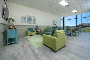 Ein geräumiges Zimmer mit großem Fenster, einem grünen Sofa, einem gemusterten Sofa sowie einem Essbereich mit Stühlen und Tisch.