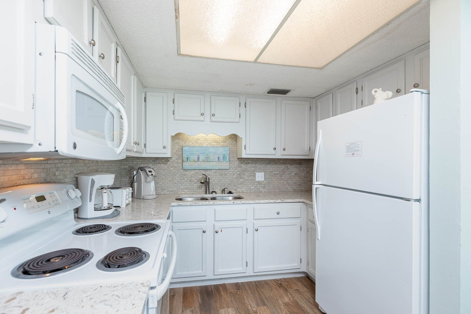 A kitchen with white cabinets, a microwave, a stove, a refrigerator, and a coffee maker.
