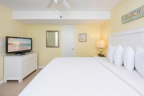 Ein Hotelzimmer mit Bett, Fernseher auf einer Kommode, Deckenventilator, Tür und Wanddeko.