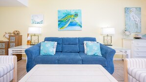 Een woonkamer met een blauwe bank, twee bijzettafels met lampen, en een schilderij van een zeeschildpad aan de muur.