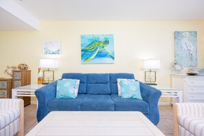 Ein Wohnzimmer mit einem blauen Sofa, zwei Beistelltischen mit Lampen und einem Bild einer Meeresschildkröte an der Wand.