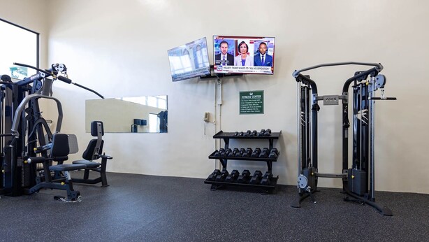 Gimnasio con equipo de ejercicio, mancuernas y una televisión mostrando noticias.