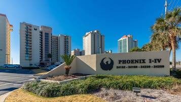 A sign for Phoenix I-IV with a bird logo, surrounded by a landscaped area with palm trees and a parking lot.