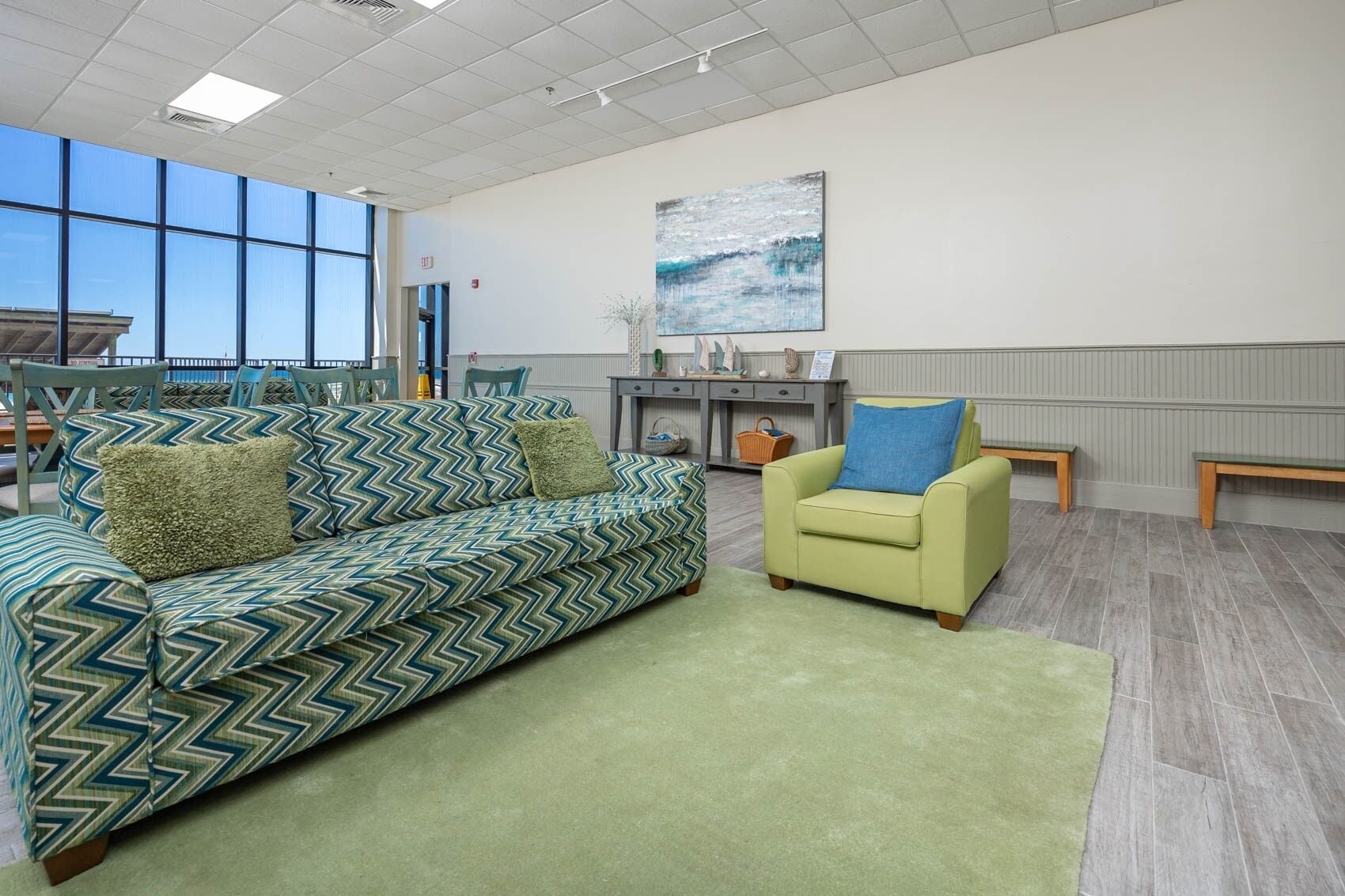 A spacious room with a large window, a green sofa, a yellow armchair, and a small table with decorative items.