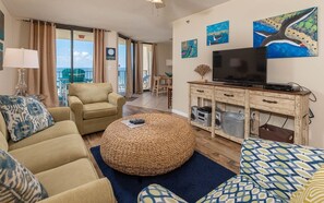 Ein Wohnzimmer mit Sofa, Hocker und Fernseher auf einem Holzschrank.
