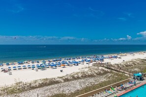Ein Strand mit vielen Sonnenschirmen und Liegestühlen, einem klaren Himmel und ruhiger See.