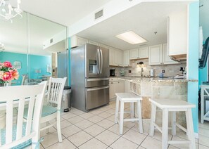 A modern kitchen with a stainless steel refrigerator, white cabinetry, and a granite countertop island. - Phoenix V 602 1 Bedroom Condo (Orange Beach)