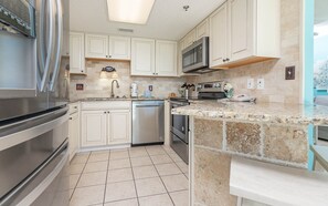 A kitchen with white cabinets, a stainless steel refrigerator, a dishwasher, a microwave, and a granite countertop. - Phoenix V 602 1 Bedroom Condo (Orange Beach)