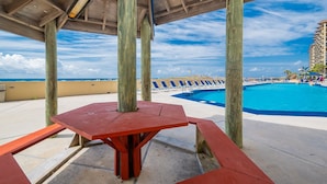 Une terrasse en bois avec une piscine et des chaises longues, offrant une vue imprenable sur un ciel bleu azur et l’océan.