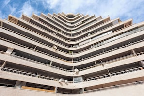 Um edifício com vários andares, varandas, um átrio central e céu azul.