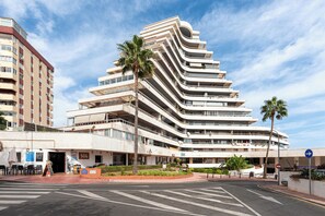 Un hotel de varios pisos con fachada curva, zona de estar al aire libre y palmeras.