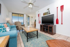 Ein Wohnzimmer mit Sofa, Sessel, Couchtisch, Fernseher und Deckenventilator.