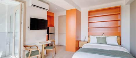 A modern hotel room with a bed, a TV, a small table with chairs, and a bathroom with a shower.
