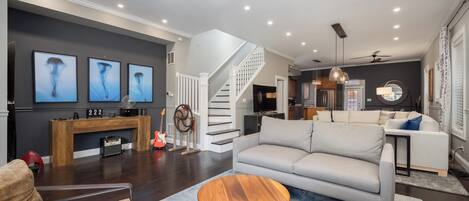 Una sala de estar moderna con un sofá gris, una mesa de centro de madera y una escalera que sube a un nivel superior.