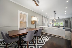A dining area with a wooden table and grey chairs, a patterned rug, and a ceiling fan.