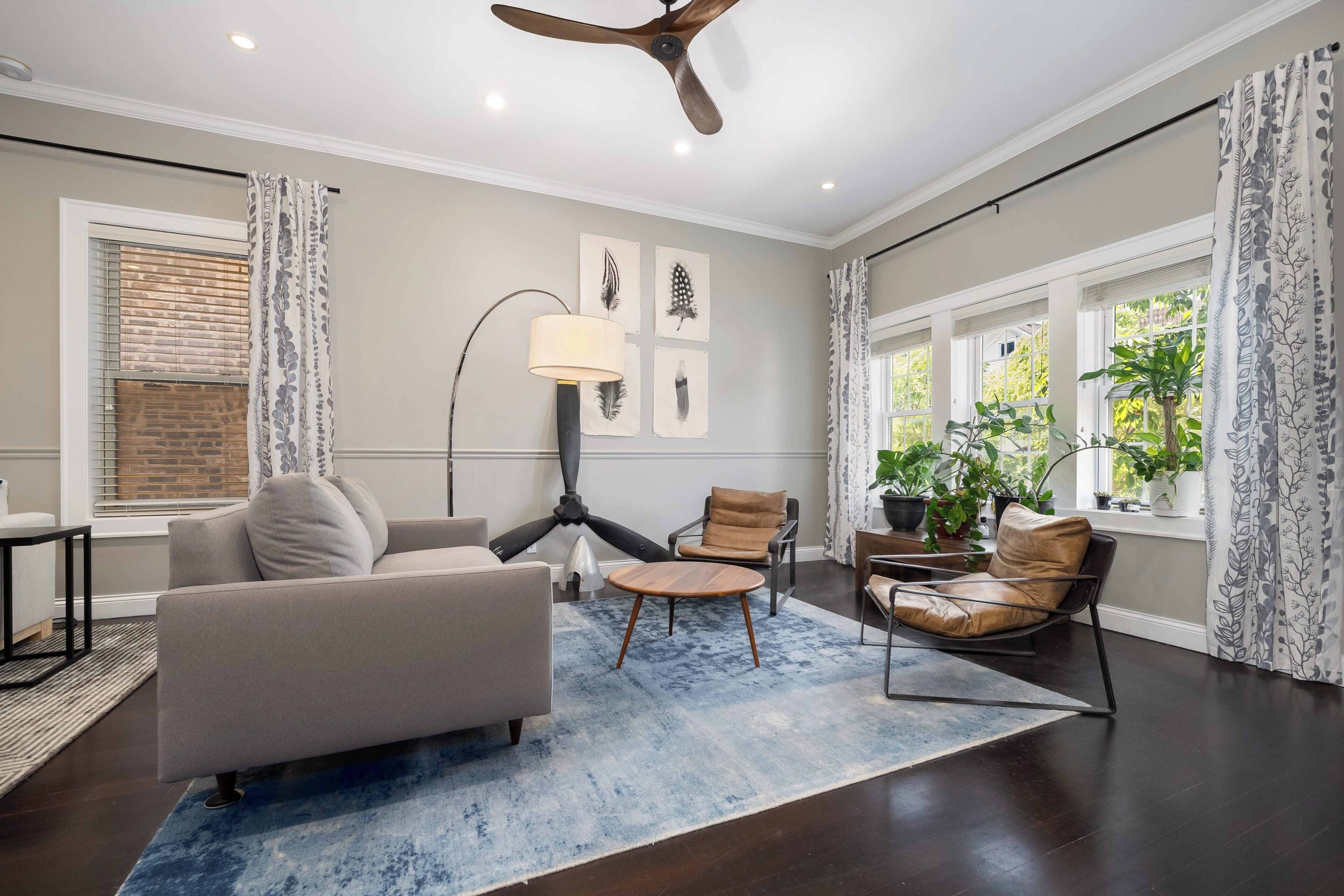 A modern living room with a ceiling fan, a sofa, two armchairs, a coffee table, and a floor lamp.