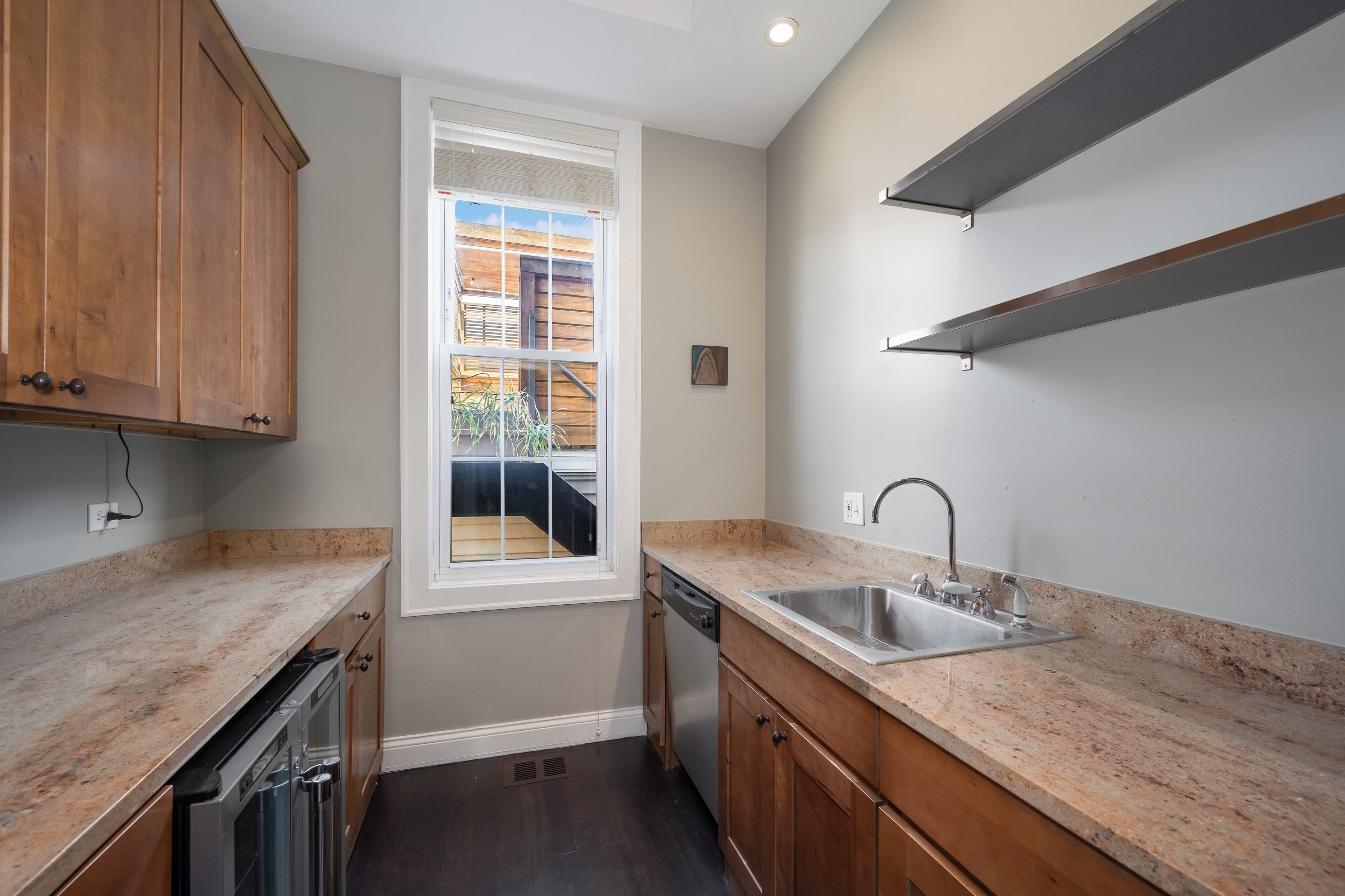 A kitchen with wooden cabinets, a built-in dishwasher, a stainless steel sink, and a window overlooking a wooden deck.