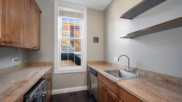 A kitchen with wooden cabinets, a built-in dishwasher, a stainless steel sink, and a window overlooking a wooden deck.
