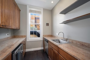 A kitchen with wooden cabinets, a built-in dishwasher, a stainless steel sink, and a window overlooking a wooden deck.