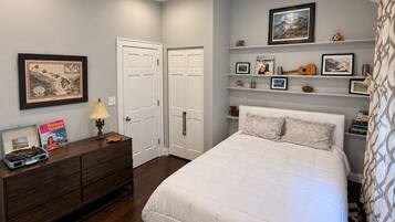 A bedroom with a bed, dresser, and shelves with framed pictures and decorative items.
