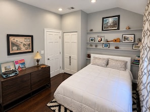 A bedroom with a bed, dresser, and shelves with framed pictures and decorative items.