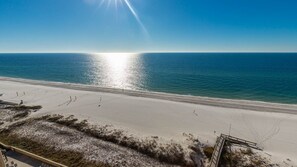 Ein Strand mit blauem Himmel, sandigem Ufer und einer hölzernen Promenade, die zum Wasser führt.