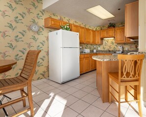 Una cocina con armarios de madera, un refrigerador blanco, una isla empotrada con un fregadero y un comedor con sillas de madera.