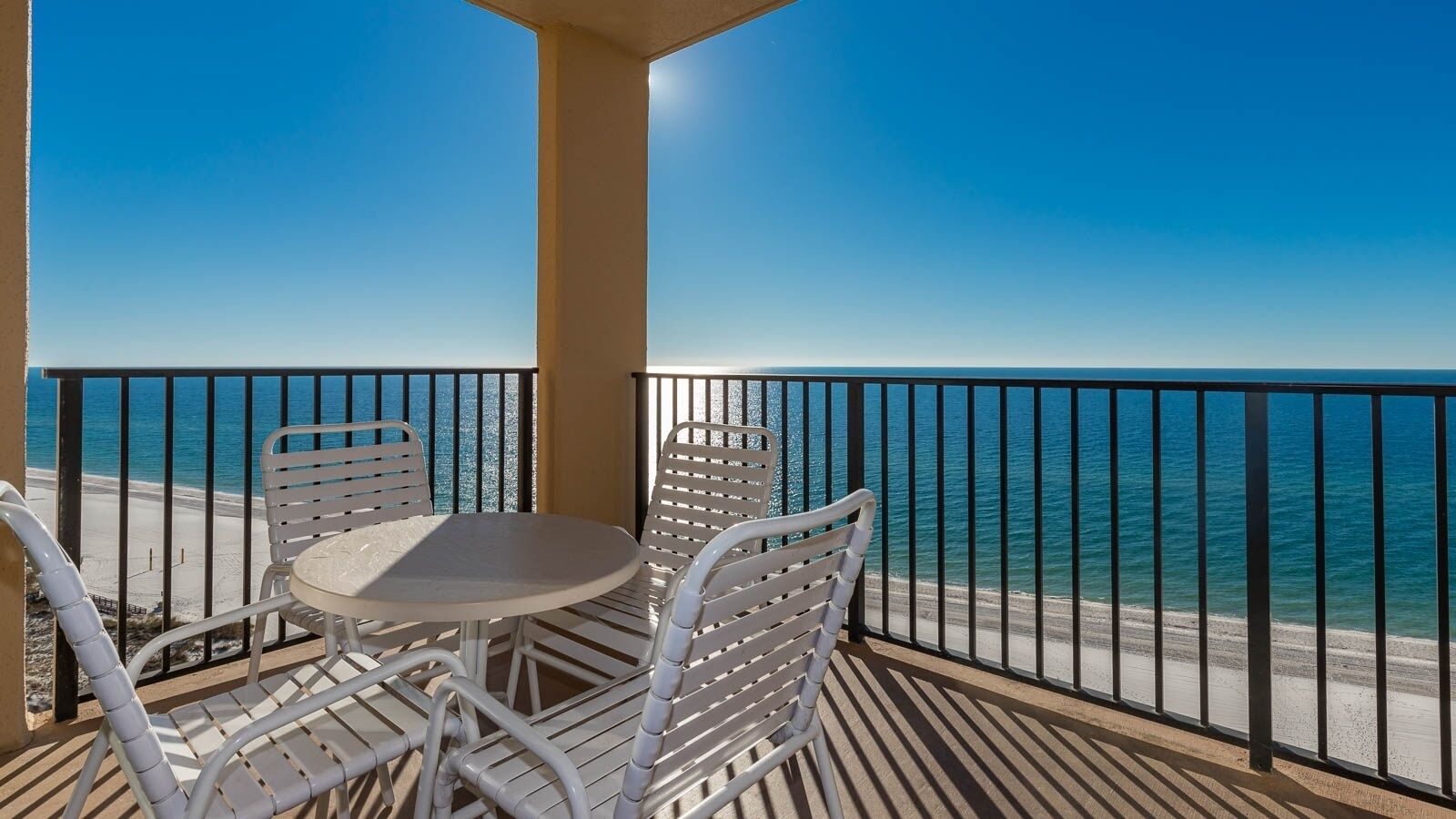 A balcony with a table and chairs, overlooking a beach and the sea.