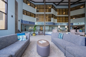 A spacious lobby with grey sofas, a round ottoman, and a tiled floor. - Phoenix V 111 1 Bedroom Condo (Orange Beach)