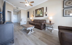 A living room with a brown leather sofa, a wooden coffee table, a television on a cabinet, and two wall-mounted lamps. - Phoenix V 111 1 Bedroom Condo (Orange Beach)