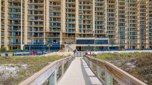 A high-rise hotel with multiple balconies, a beachside walkway, and a pool area with blue chairs. - Phoenix V 111 1 Bedroom Condo (Orange Beach)