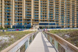 A high-rise hotel with multiple balconies, a beachside walkway, and a pool area with blue chairs. - Phoenix V 111 1 Bedroom Condo (Orange Beach)