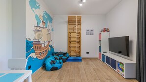 Una habitación con piso de madera, una televisión de pantalla plana grande, una estantería, una pared con un mural de un mapa y un sillón informal azul.