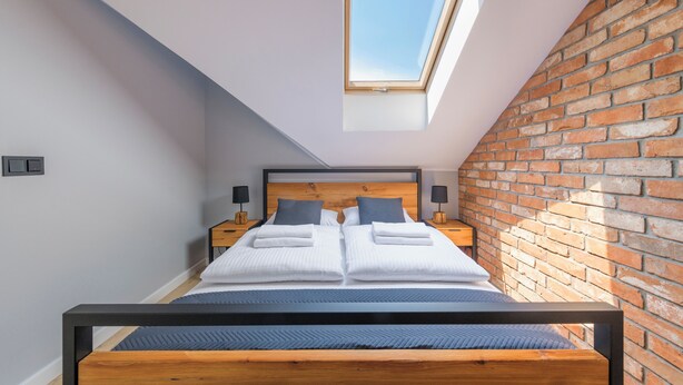 Un dormitorio con tragaluz, pared de ladrillo y cama con almohadas y manta.