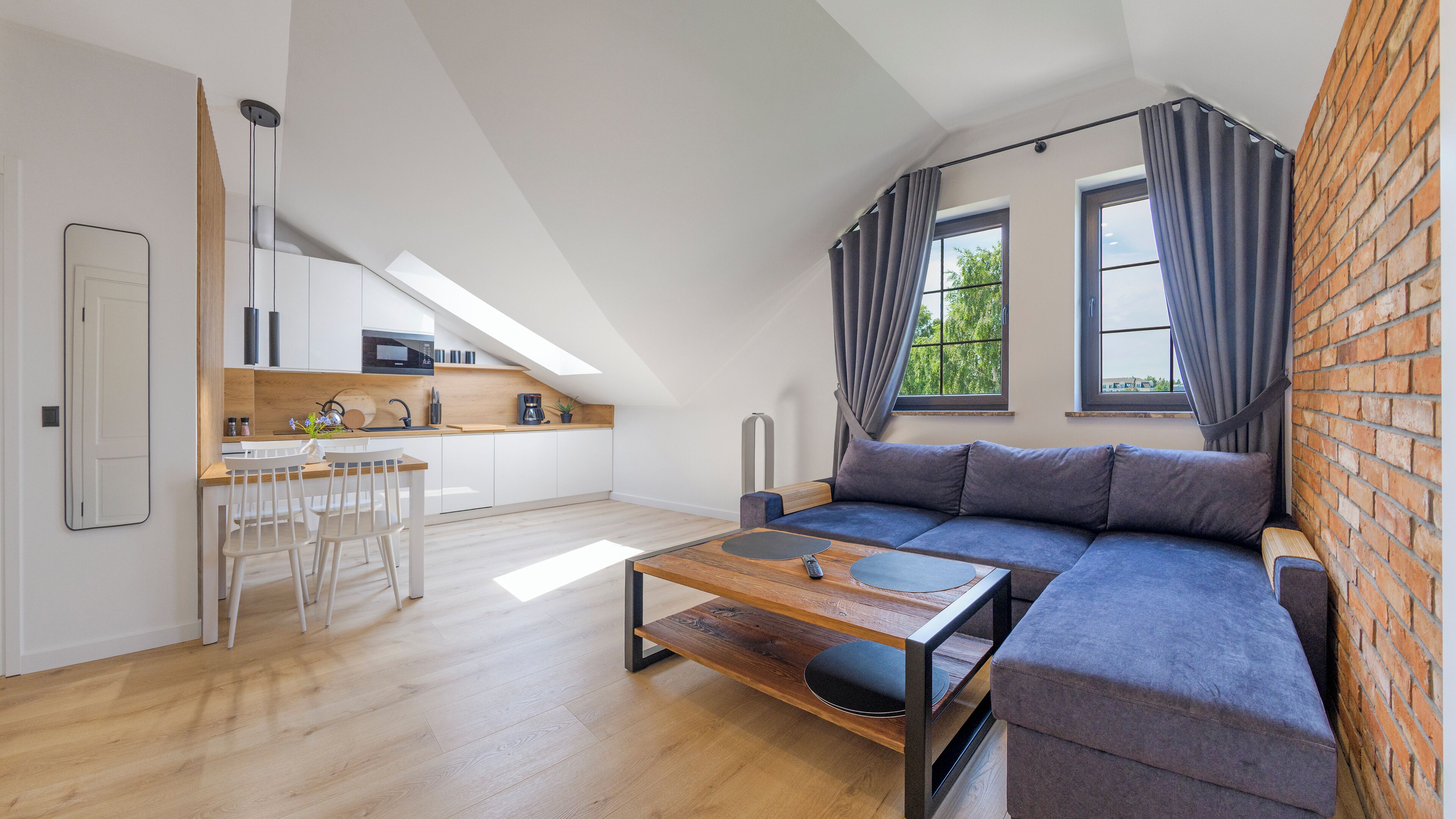En modern lägenhet i loftstil med ett matområde, kök och ett stort fönster med gardiner.
