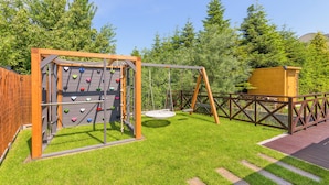 Un parque infantil con muro de escalar, columpios y una casita de madera.