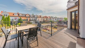 Una terraza de madera con mesa y sillas, una barandilla metálica y vistas a casas vecinas.