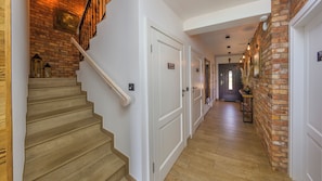 A wooden staircase leading to a landing with a white door, a brick wall, and a hallway with a wooden floor. - Apartamenty Sun & Snow Salt&Wood (Łeba)