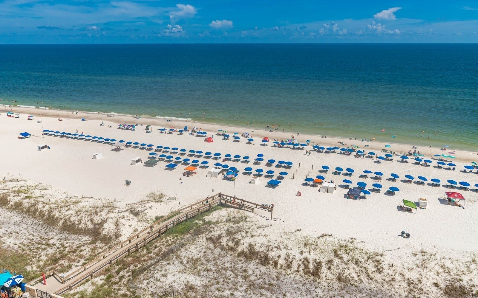 A beach with rows of umbrellas and beach chairs, a wooden boardwalk, and the ocean in the background.