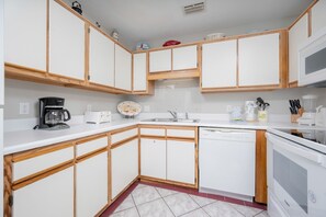 A compact kitchen with white cabinets, a coffee maker, a toaster, a sink, and a dishwasher. - Phoenix V 1414 1 Bedroom Condo (Orange Beach)
