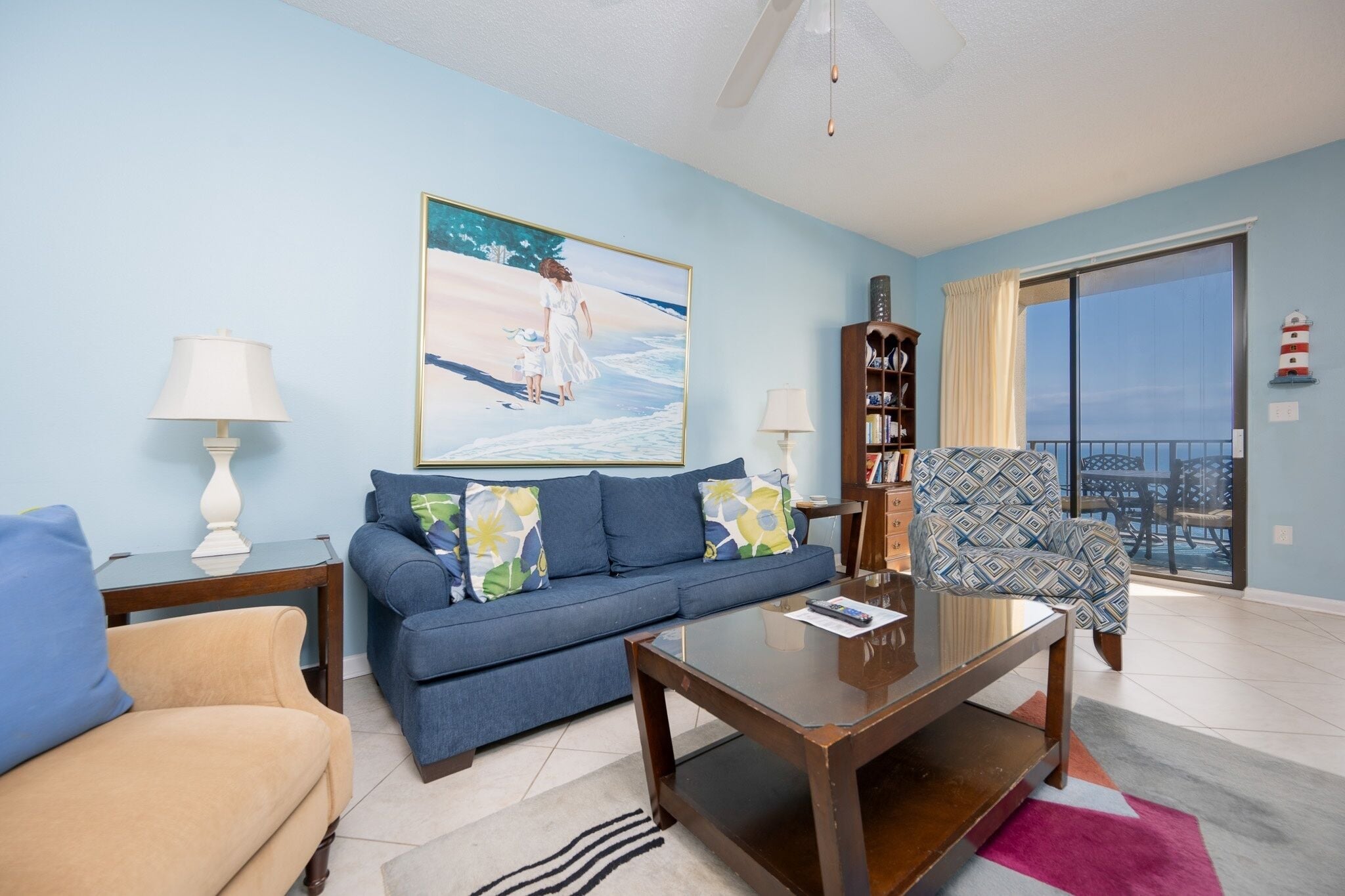 A living room with a sofa, a coffee table, a bookshelf, and a painting of a beach scene.