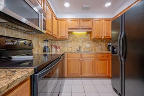 A kitchen with wooden cabinets, a stainless steel refrigerator, a built-in oven, and a granite countertop. - Phoenix I 1146 1 Bedroom Condo (Orange Beach)