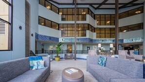 Eine geräumige Lobby mit grauen Sofas, einem runden Ottomanen und einem gefliesten Boden.
