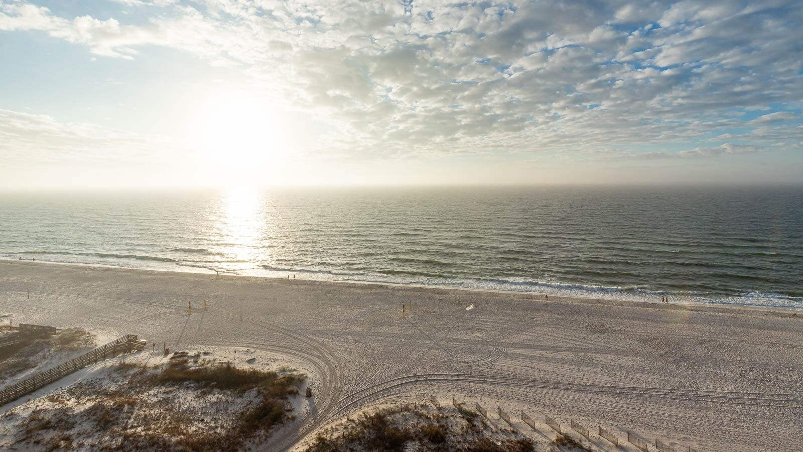 Een strand met een houten looppad naar het water, een heldere lucht en de zon die aan de horizon onder- of komt op.