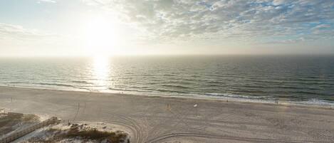 Een strand met een houten looppad naar het water, een heldere lucht en de zon die aan de horizon onder- of komt op.