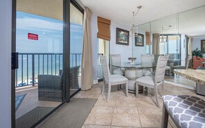 A balcony with a glass door leading to a beach view, a round glass table with chairs, and a sofa with a patterned cushion. - Phoenix V 914 1 Bedroom Condo (Orange Beach)