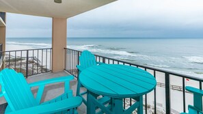 Ein Balkon mit türkisfarbenen Stühlen und einem Tisch mit Blick auf einen Strand und Wellen.
