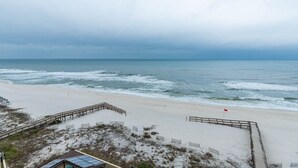Ein Strand mit einer Holzpromenade, die zum Wasser führt, feinem Sand und einem bewölkten Himmel.